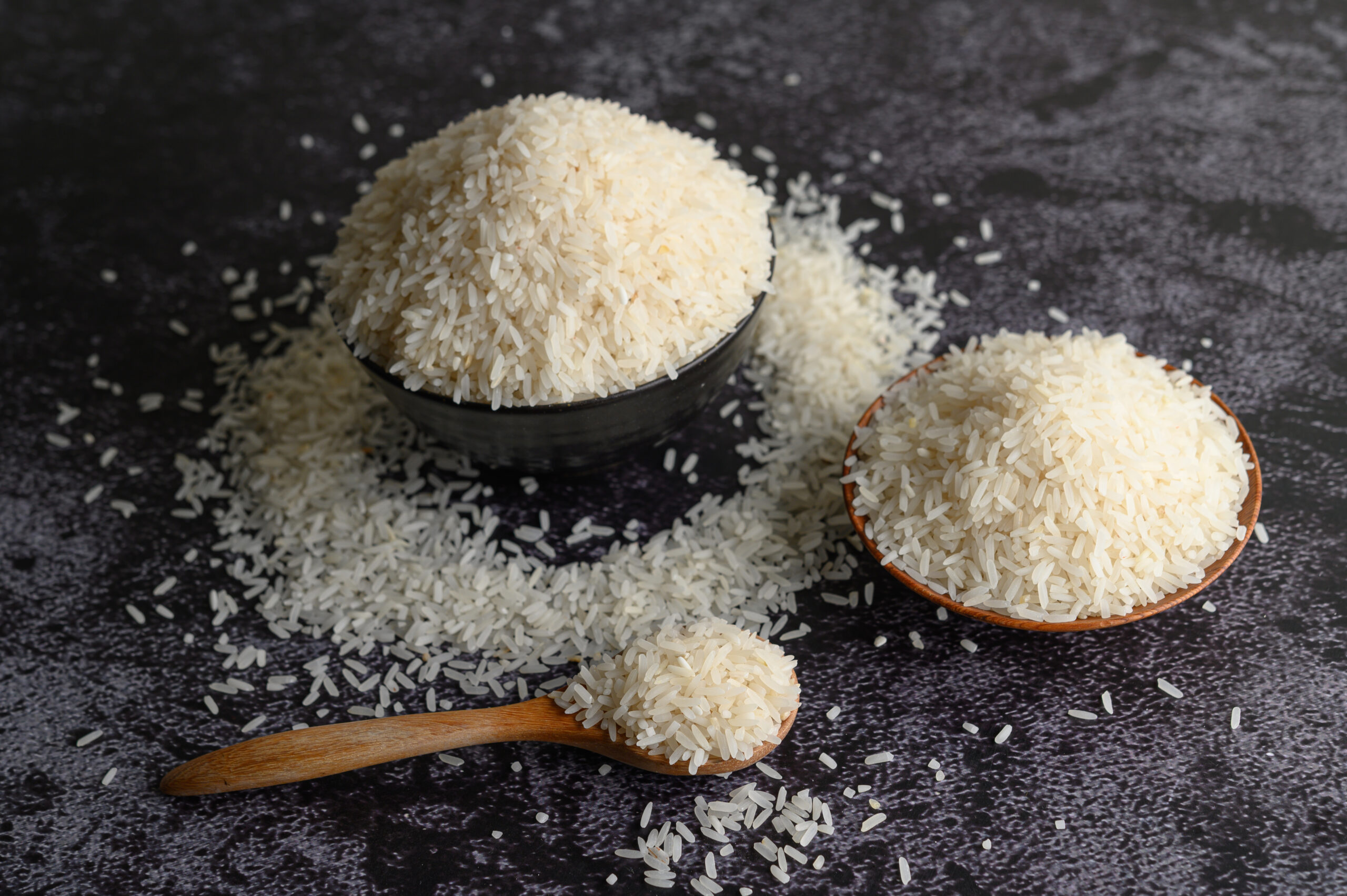 Milled rice in a bowl and a wooden spoon on the black cement floor. Selective focus